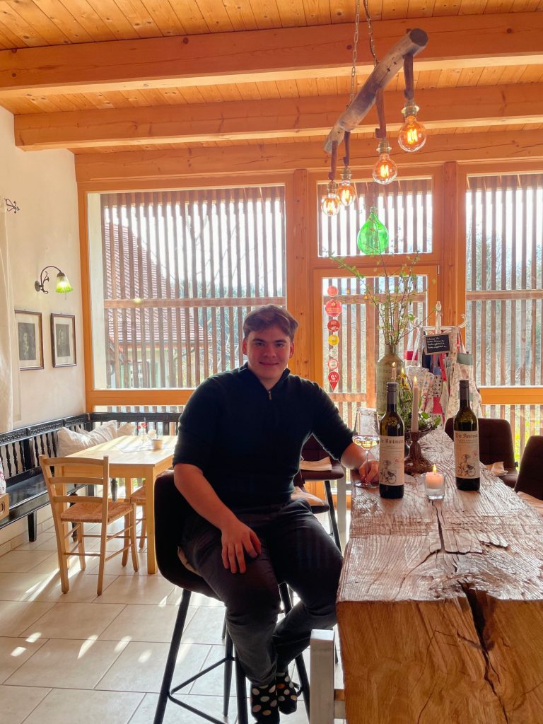 Der Sohn der Familie sitzt auf einem Barhocker im Genussladen