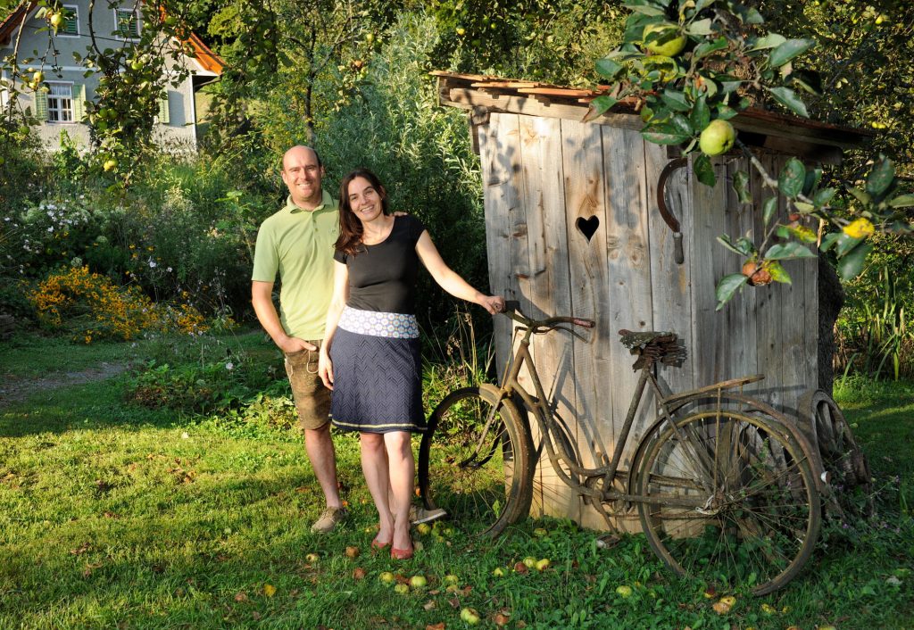 Markus und Franziska Skoff im Garten vor einem Fahrrad, im Hintergrund das Haus