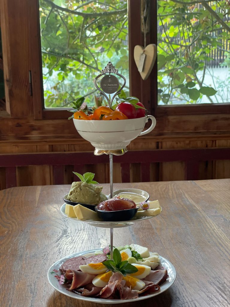 Frühstücksplatte mit Wurstwaren, Käse und bunten Beilagen auf einem rustikalen Holztisch.