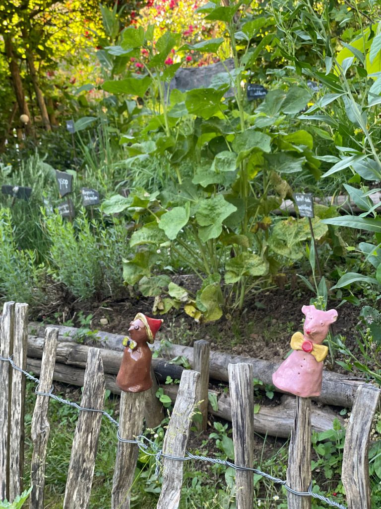 Pflanzen aus dem Garten im Detail, davor ein Holzzaun mit Tonfiguren