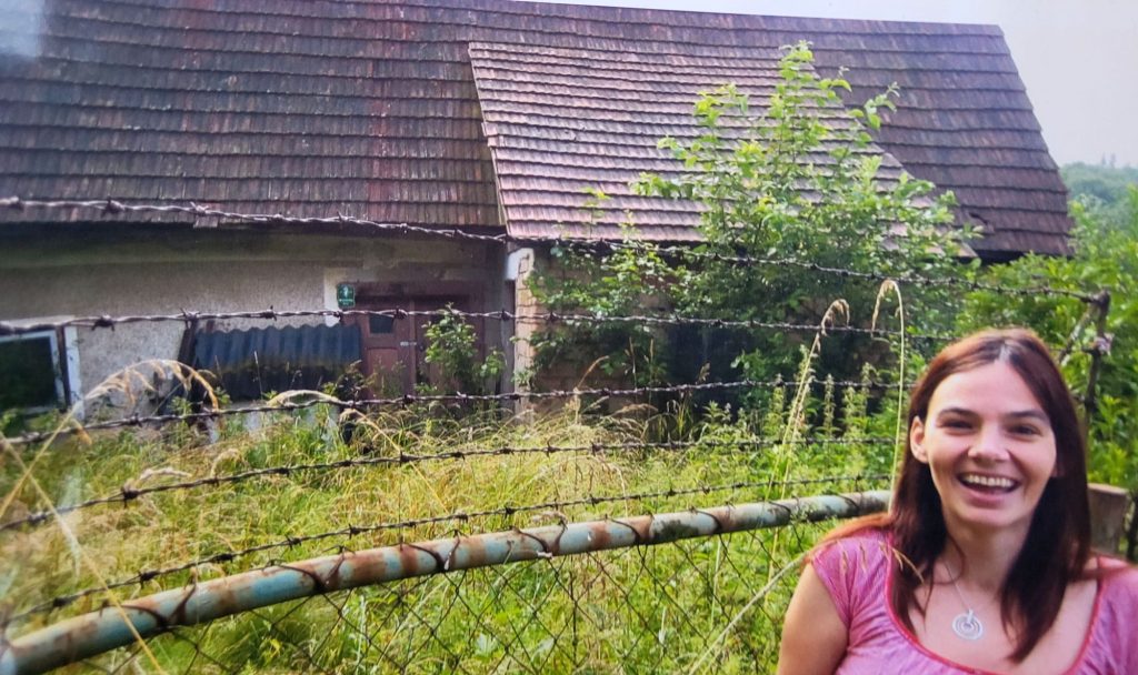 Lächelnde Frau vor alten Haus mit Zaun und bewachsene Landschaft