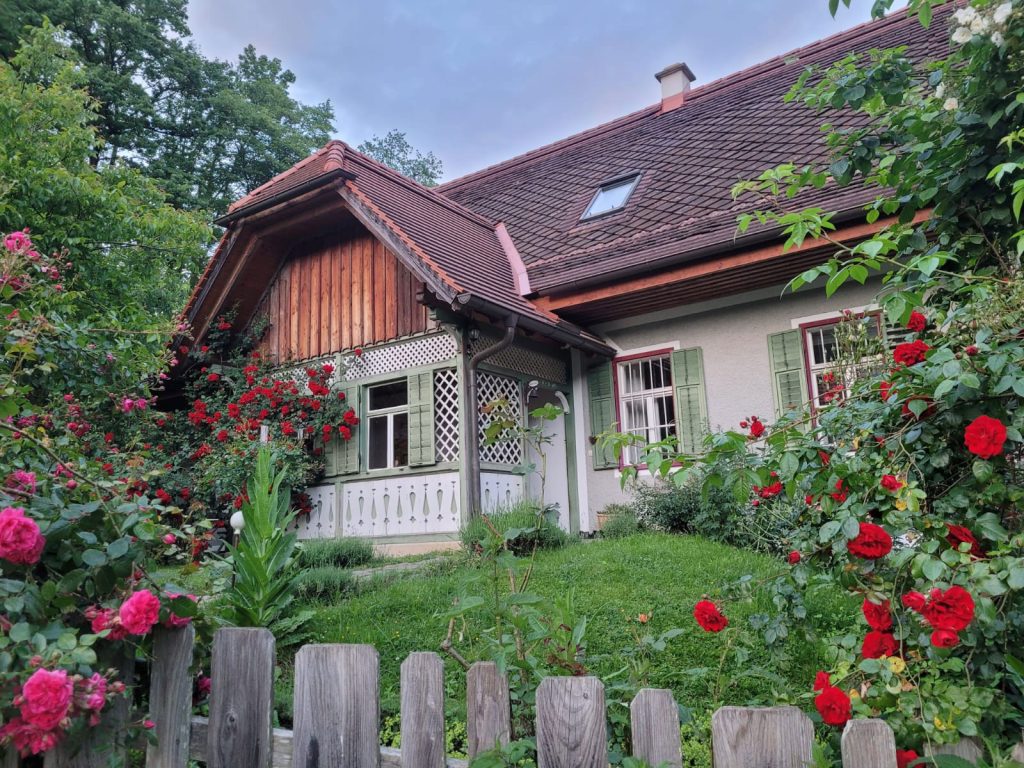 Ein charmantes Häuschen mit roten Rosen, grünen Fensterläden und einem verwitterten Holzzaun.