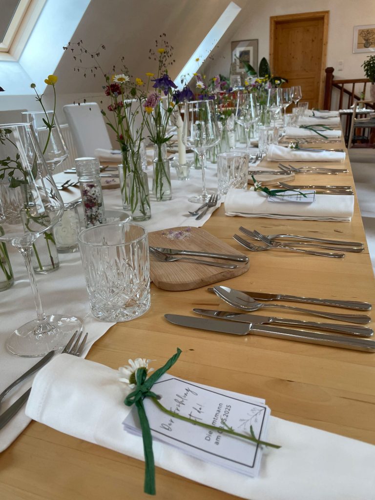 Gedeckte Tafel mit Wiesenblumen in Vasen am Tisch