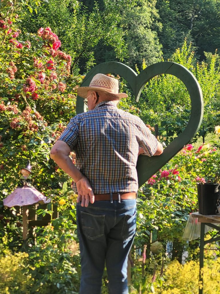 Ein älterer Herr stützt sich auf grünem Holzherz ab